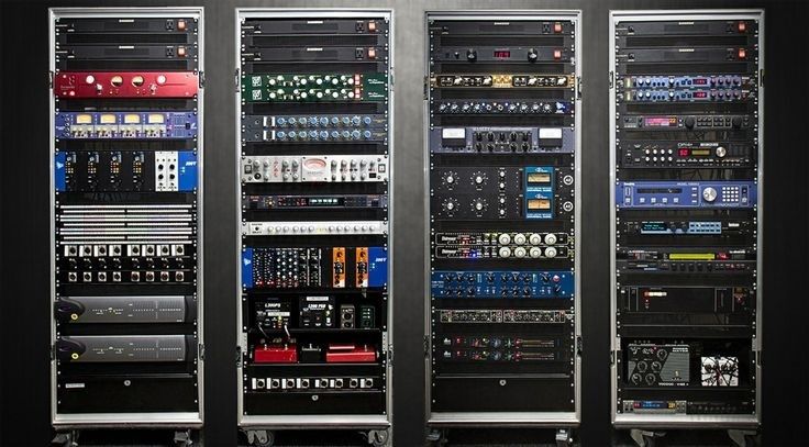 Vier dicht bestückte Studio-Racks mit zahlreichen Audiogeräten und Kabelanschlüssen