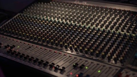 Nahaufnahme eines beleuchteten Audiomischpults mit vielen Reglern